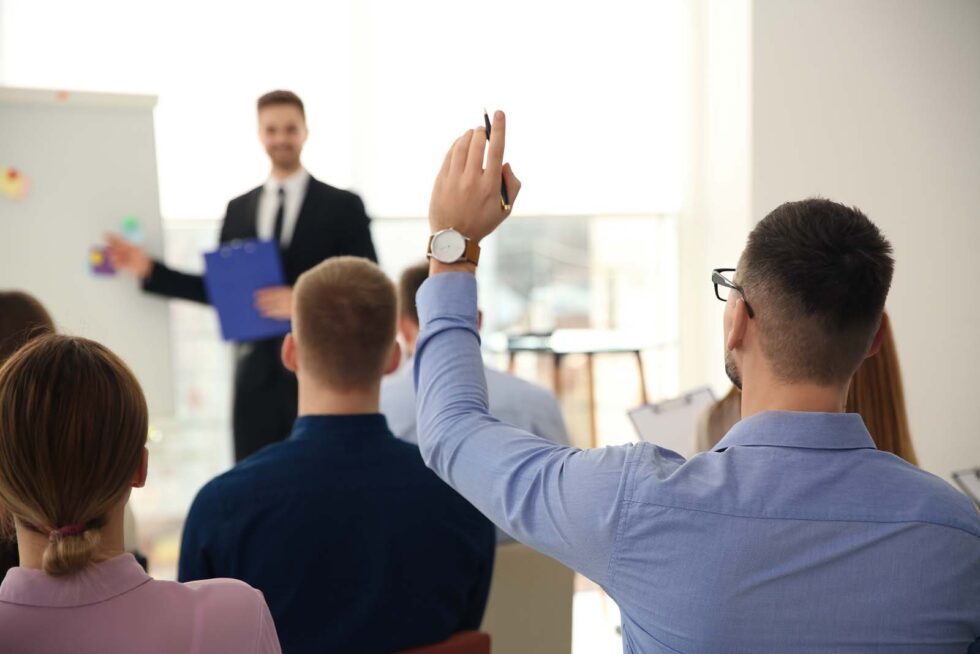 Man raising hand to ask question at business training indoors